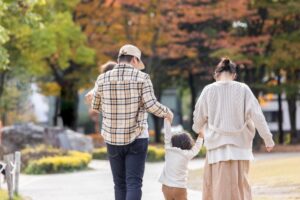 公園の並木道を歩く家族の後ろ姿。遺族年金は2028年4月に改正され、受け取れる期間が世帯によって変わる