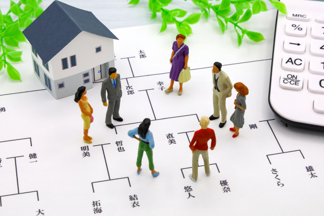 家系図の上に家族の人形が並び、そばに家の模型と電卓が置かれている
